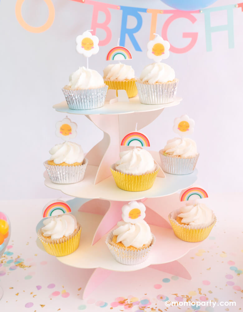 Cupcakes with Party Deco Rainbow and Daisy Birthday Candles as cupcakes toppers, on a Talking Tables Pastel rainbow We Heart Pastels Cake stand, with Meri Meri Multicolor Letter Garland Kit spells " To brighter Day" text behind it, and Cupcake Artisan Confettis on the table, for a Good vibes birthday party, a rainbow themed birthday, "Happy Day" themed celebration!