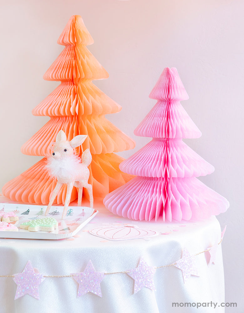 Pastel Pink Christmas party table set up with Devra Party Peach and light pink Honeycomb Paper Christmas Trees, a cute deer ornament decoration, Fa la la christmas tree plate with tree cookies on a kid table, and StudioPep Pink Glitter Star Banner on the side of the table for a cozy celebration