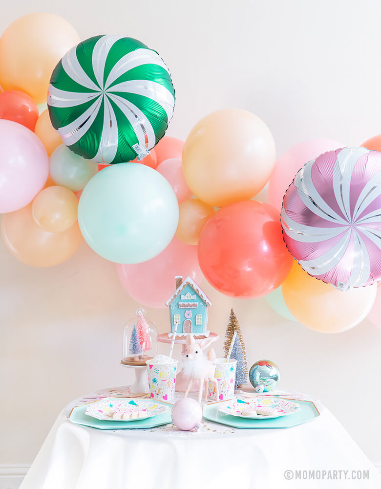 Merry & Bright Christmas Holiday Boxes with Pastel Color themed mint, peach, pink balloon garland and Satin candy swirls foil balloon as backdrop, Meri Meri Mint Large Dinner Plates, and Day dream societyMerry and Bright Small Plates, Napkins and Cups as tablewares for a modern cute pastel holiday party idea