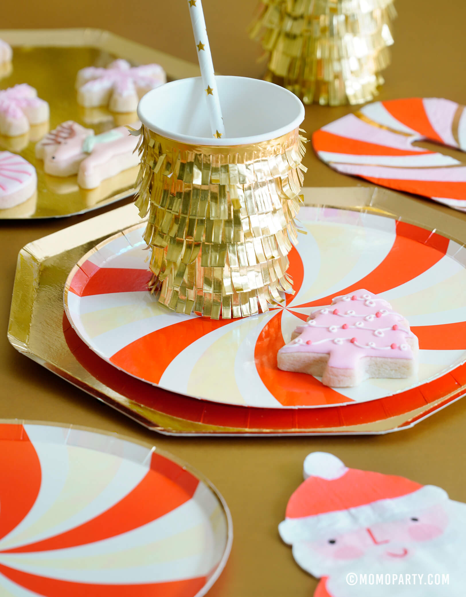 Modern Meri Meri Gold Fringe Party Cup with Gold Large Dinner Plates, and Peppermint Swirl Side Plates and Santa Napkin for a Gold Red Peppermint Glam Christmas Celebration with Meri Meri Gold Fringe Party Cup with Gold Large Dinner Plates, and Peppermint Swirl Side Plates and Santa Napkin and pastel christmans tree shaped cookies. 