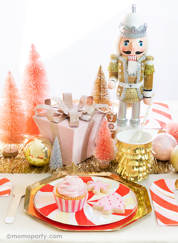 Momo party Holiday tablescape look with cupcake and pink christmas tree cookie, pink snowflake cookie on the  Peppermint Swirl Side Plates layered on top of Gold Large Dinner Plates, gold fringe cups and peppermint napkin on the side. with a pink christmas gift box, pink and gold Sisal Trees and a Nutcracker as centerpiece, ready for a modern classic look of Gold Red Peppermint Glam Christmas party Celebration