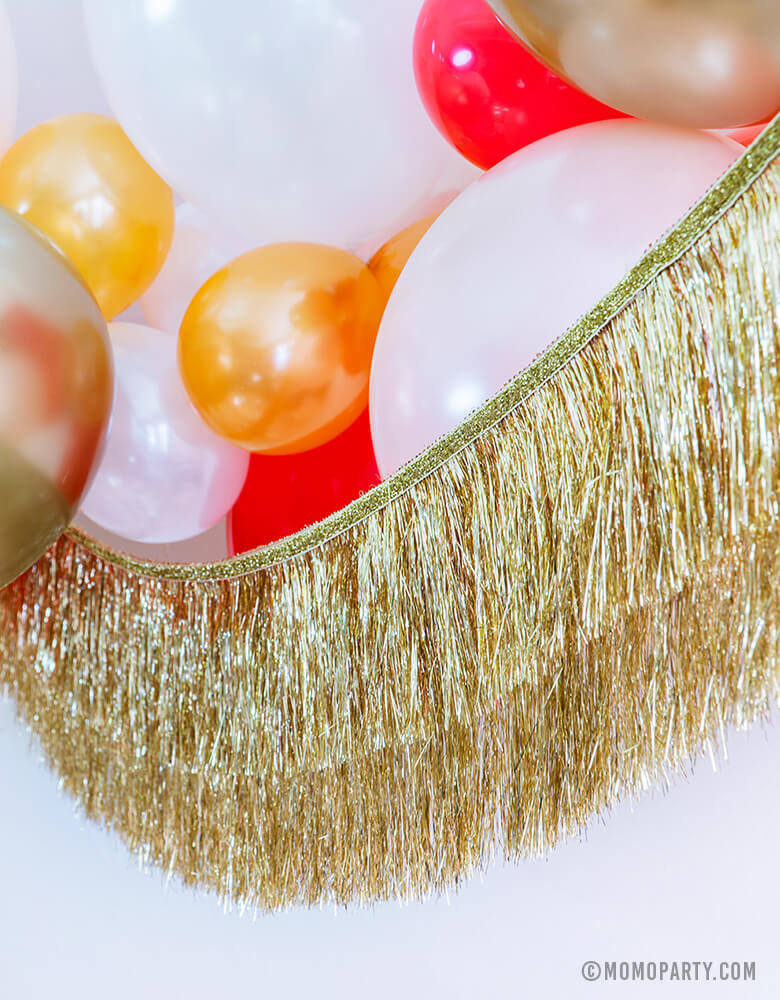 Momo Party Holiday party decoration idea feathered Gold, Red, Pearl White, Coral, Pearl peach latex balloons with Meri Meri gold tinsel fringe garland