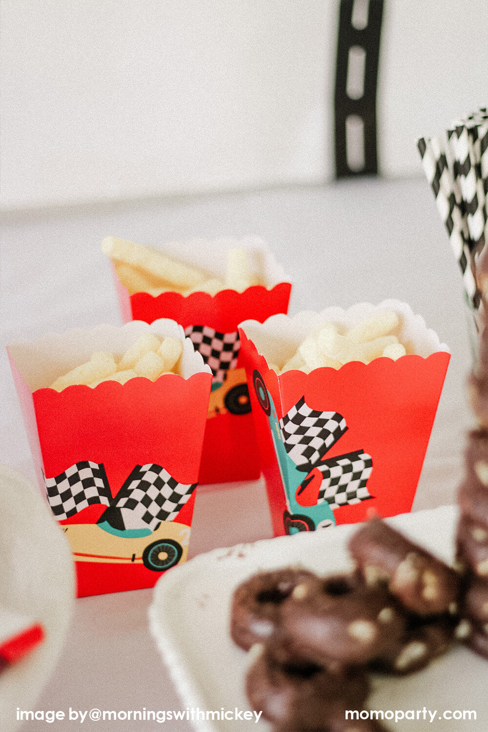 Race Car-themed Birthday party table close-up of, Red paper cups decorated with Merrilulu Race Car Gift Bag Stickers with chips as party snacks.These stickers feature vintage red, blue and yellow race car with checkerboard flag design. peel and stick on a paper bag, or popcorn cups ready for a modern race car party decoration. This modern Race Car Birthday party hosted by Momo Party with Mornings-with-Mickey is so fun for kids who love Disney Cars, Race Car and 2nd birthday