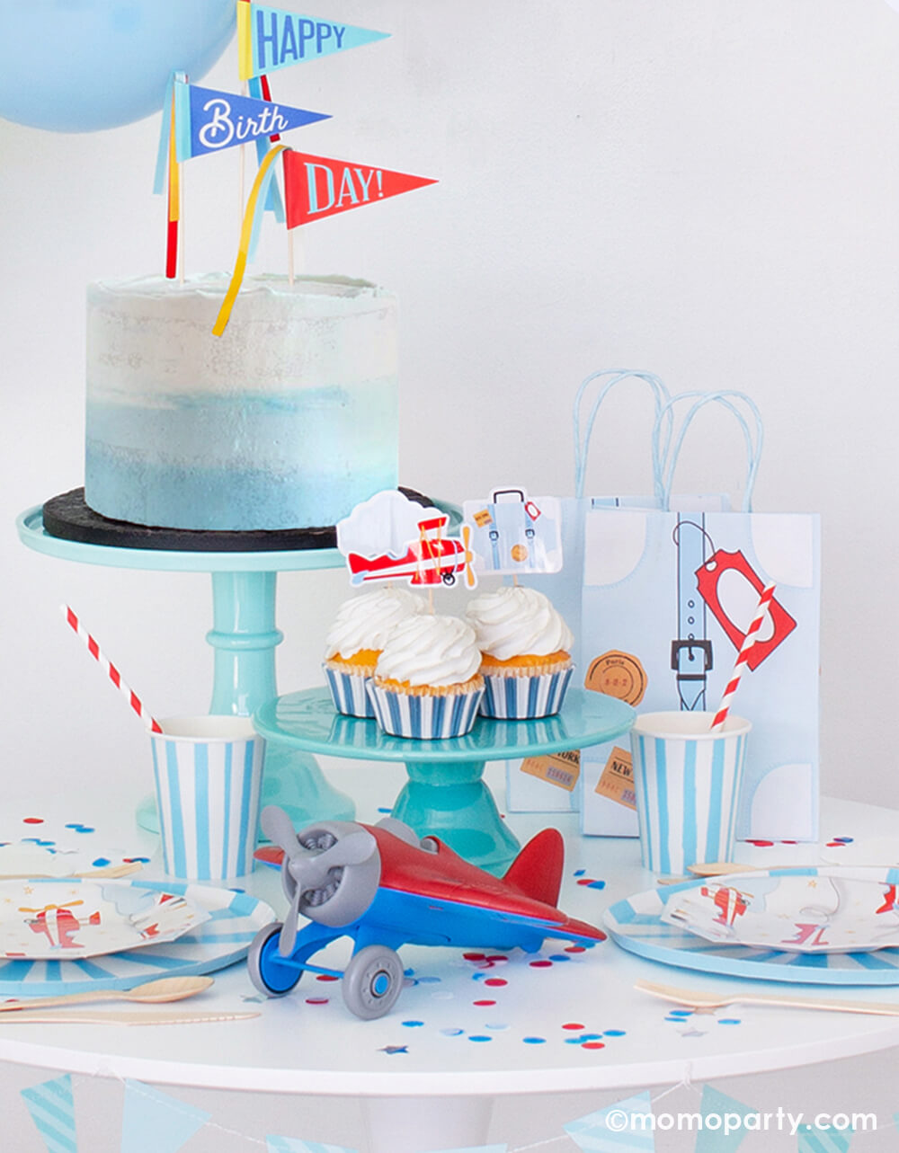 Airplane themed party with a light blue naked cake on a blue cake stand, a airplane toy, Airplane Small Plates layered with blue stripe plates, cupcakes decorated with Airplane Toppers, Airplane Party Bags and confetti on the table. Super cute set up for a airplane birthday party
