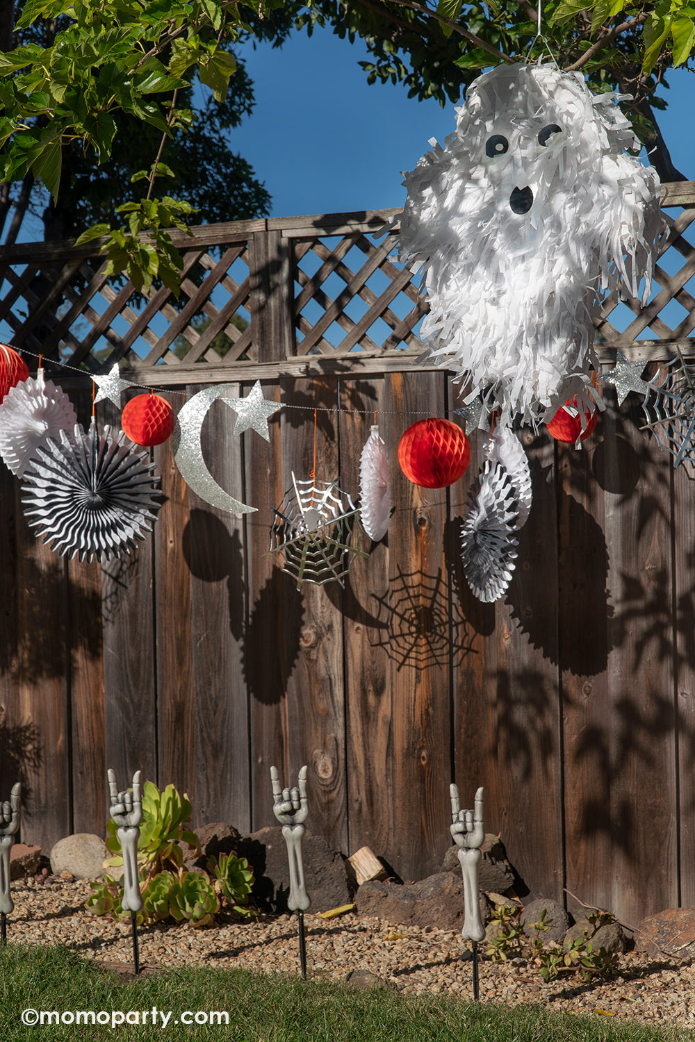 A backyard Halloween party featuring Meri Meri's 6 ft Halloween honeycomb garland hung over the fence, next to a ghost shaped Pinata for a fun kid's Halloween party. This set of garland includes a combination of stars, cobwebs, spiders, pinwheels, a crescent moon, honeycomb balls and lots of shimmering glitter, all in all makes an amazing decoration for a spooky fun Halloween celebration.