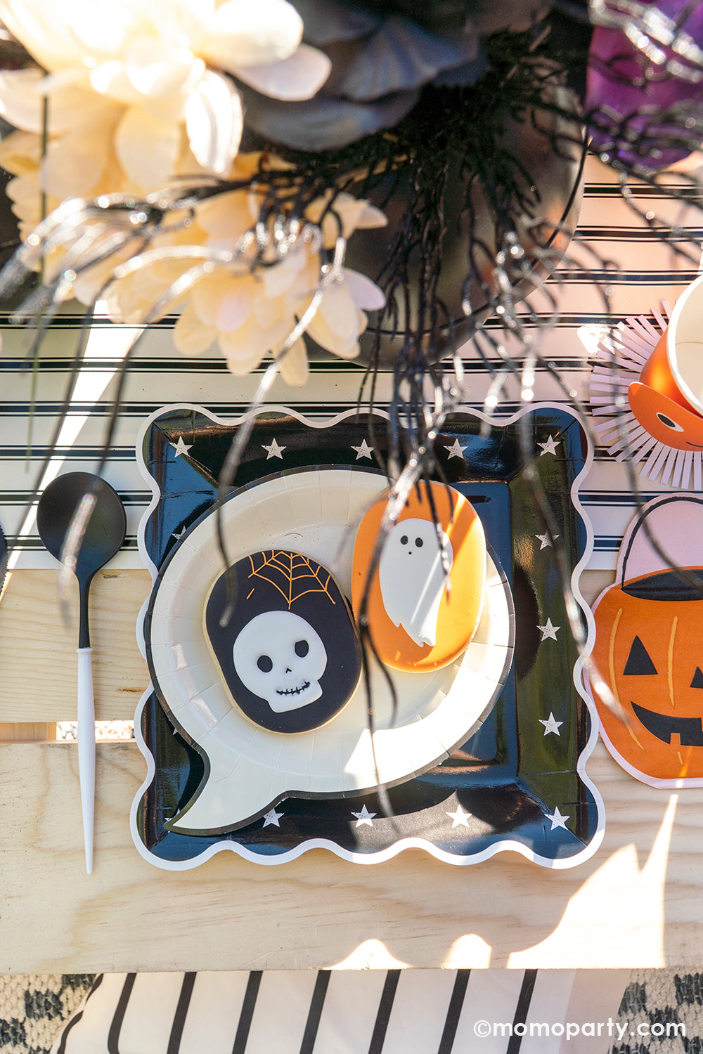 A spooky fun kid-friendly Halloween tablescape featuring My Mind's Eye's Night Sky Scalloped plates, Happy Haunting Boo Small Plates with had two matching Halloween themed sugar cookies on them, along with Jack o' Lantern pumpkin bucket shaped napkins and Meri Meri's Vintage Halloween party cups, on My Mind's Eye's black and white striped table runner, all makes a spook-tacular Halloween celebration inspo!