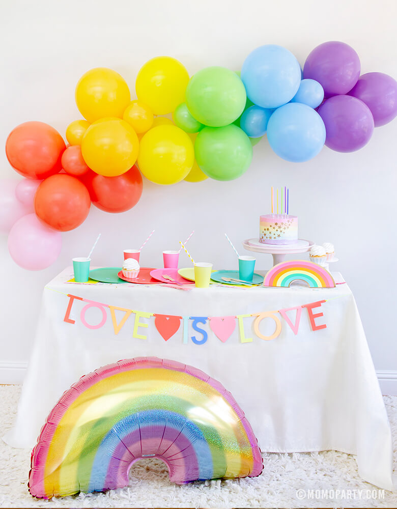 Rainbow theme Pride Party, with Meri Meri Multicolor Letter Garland Kit with message of "love is love" in front of rainbow themed dessert party table and HOLOGRAPHIC PASTEL GLITTER RAINBOW FOIL MYLAR BALLOON