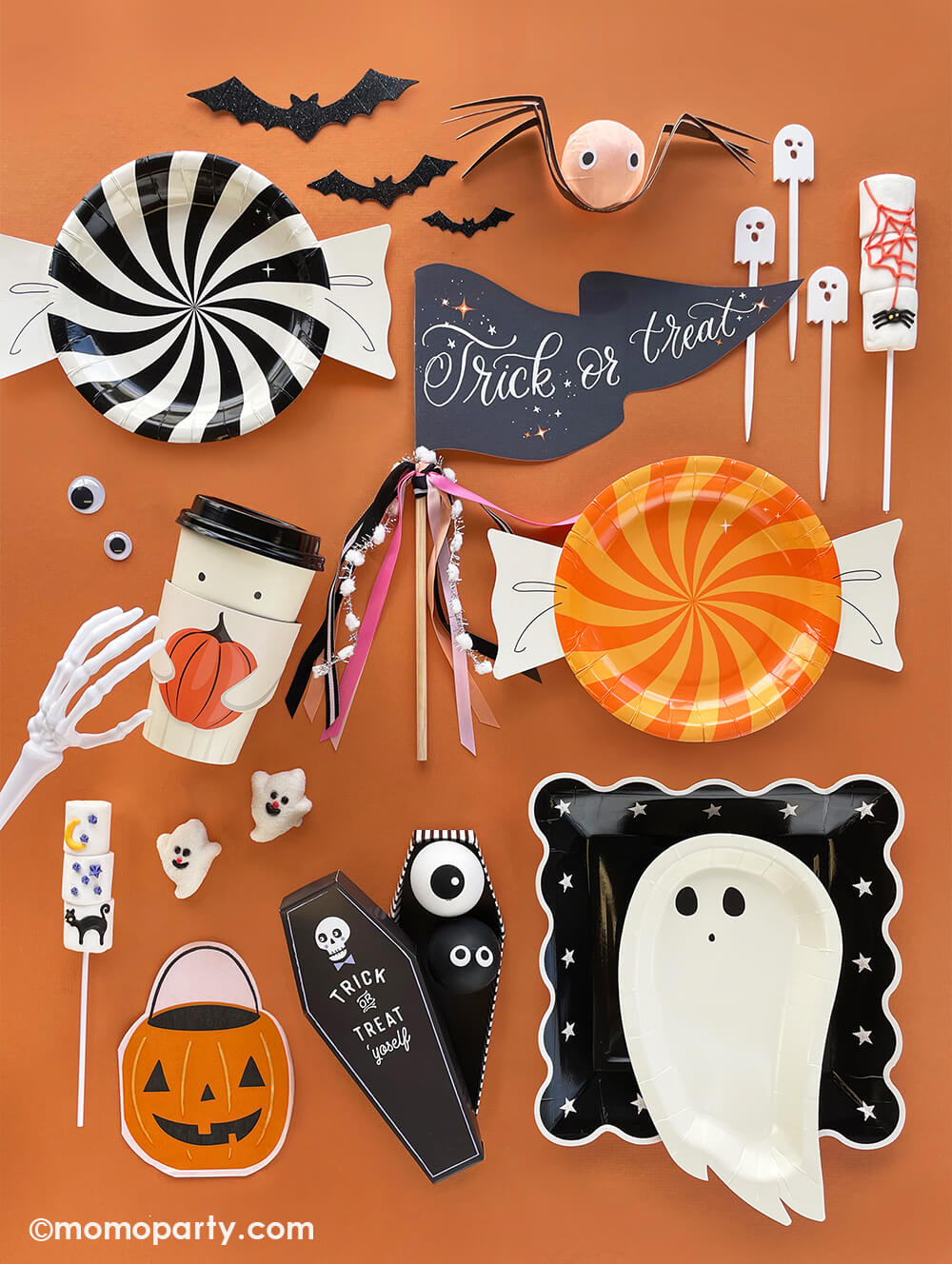 Kids Halloween Party Ideas consist of a table filled with modern and fun Halloween themed party supplies including ghost shaped plates, a trick or treat party pennant, ghost shaped acrylic stirrers, ghost shaped marshmallow, pumpkin bucket napkins, trick or treat candy shaped plates and bat decorations, all ready for a spooky fun night this Halloween!