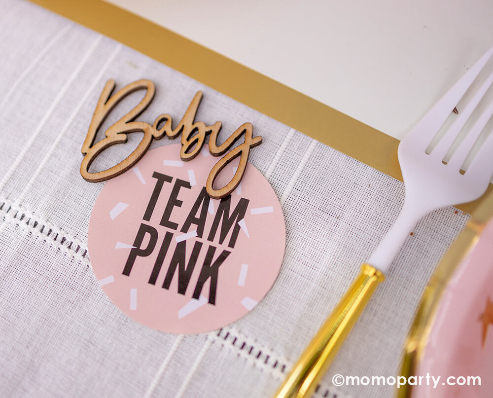 Oh baby! A gender reveal party table decorated with Ginger Ray's wooden baby confetti  next to a "team pink" sticker - a great idea for a fun gender reveal party
