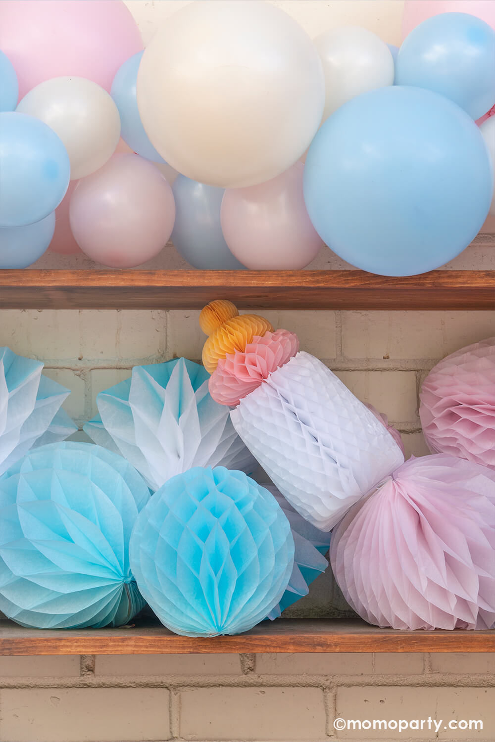 Boy or girl? A gender revel party by Momo Party, a brick wall decorated with script foil letter balloons and a wall filled with honeycomb decorations in pink and blue and a boho pastel color balloon garland in baby pink and baby blue colors