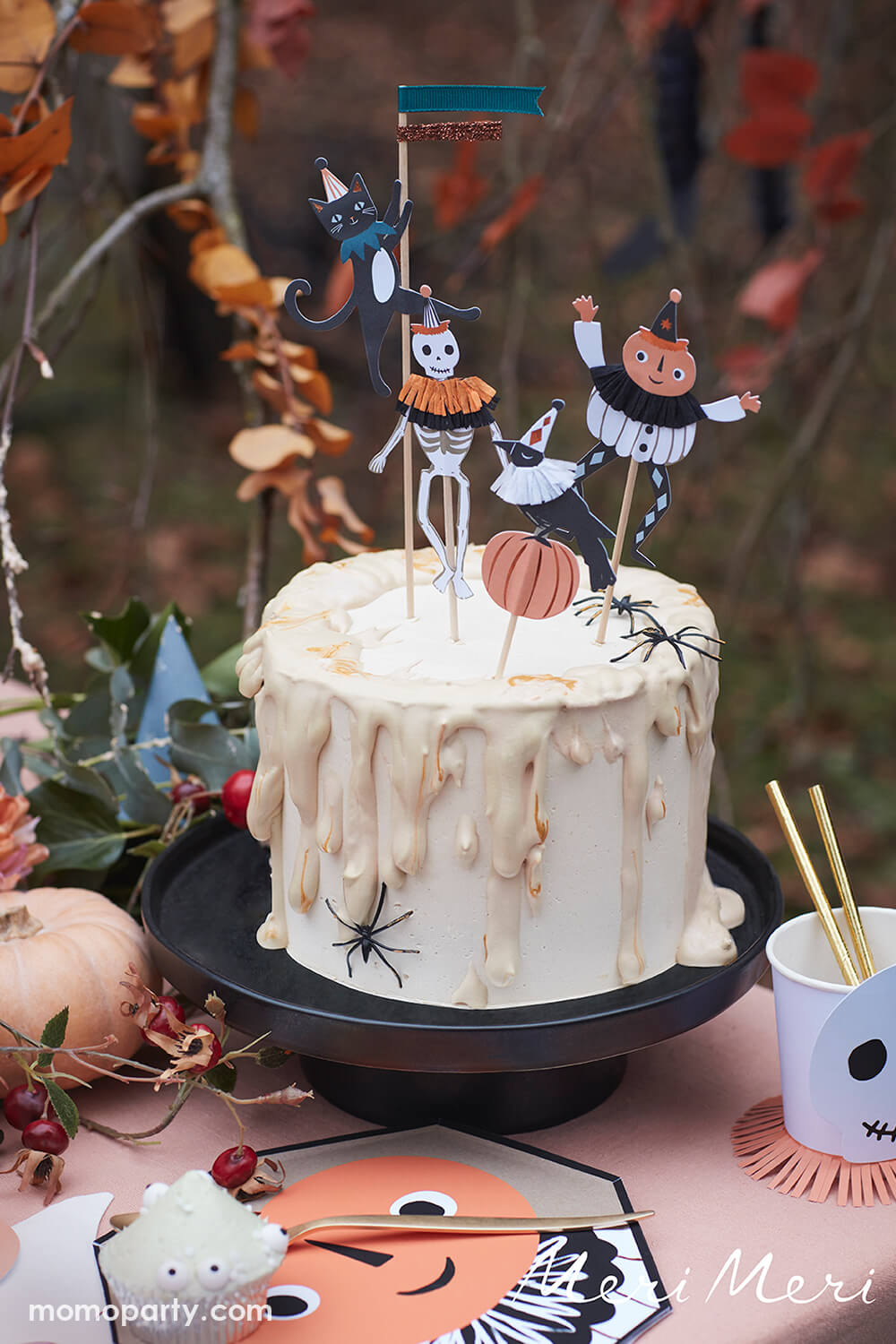 Classic Spooky Halloween party cake decorated with Meri Meri Vintage Halloween Cake Toppers, in pumpkin, crow, black cat and skeleton designs. Featuring ruffles around their necks made from crepe paper, and a spider decoration in the side of the cake. There are Vintage Halloween Side Plates with cupcakes on it, a vintage cups in skull design with gold straws on the table. inspiration from the roaring ‘20s to create a decadent new collection, this vintage halloween collection are perfect for halloween party