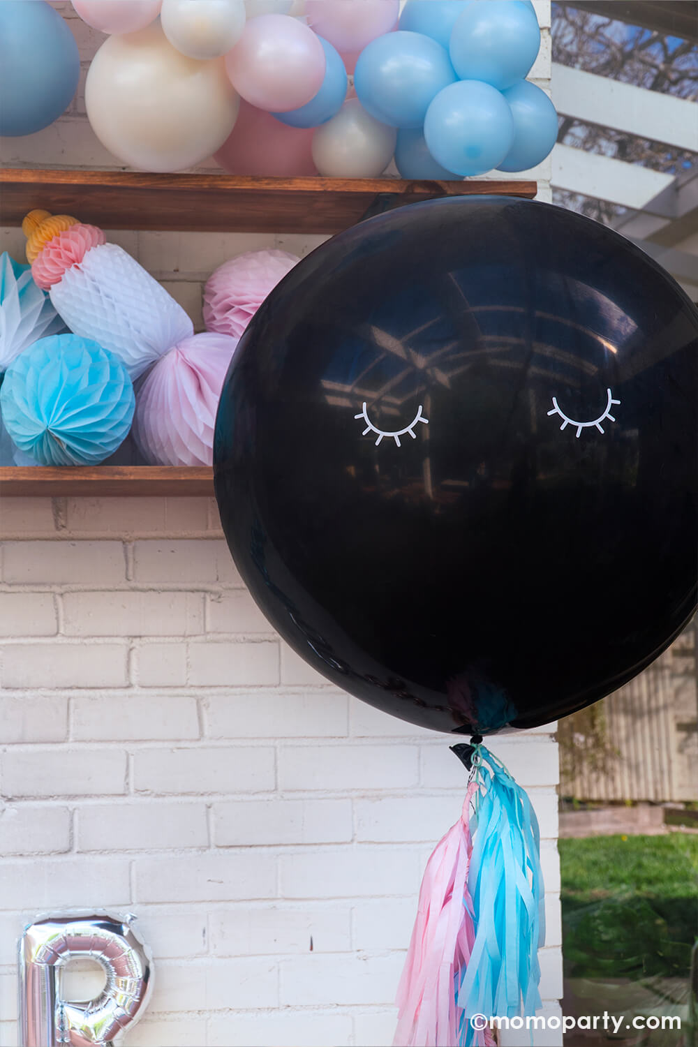 Boy or girl? A gender revel party by Momo Party, a brick wall decorated with script foil letter balloons and a wall filled with honeycomb decorations in pink and blue and a boho pastel color balloon garland in baby pink and baby blue colors. In the front is the jumbo gender reveal confetti balloon decorated with pink and blue tassel, ready to be popped to reveal baby's gender!