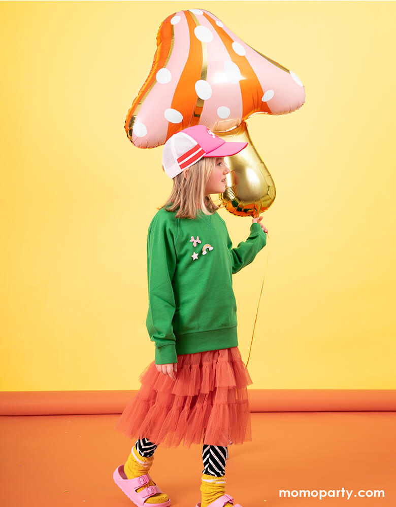 Kid holding a unique Mushroom shaped Foil Mylar Balloon with a colorful background. Decorate your woodland or fairy themed party with this whimsical mushroom shaped foil balloon!
