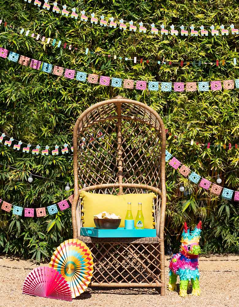 My-Minds-Eye-Fiesta-Mini-Banner-Set with ticker tape banner, llama banner, papel picados banner and mini cactus banner hung on top in a fiesta themed party with colorful decorations including party fans and piñata