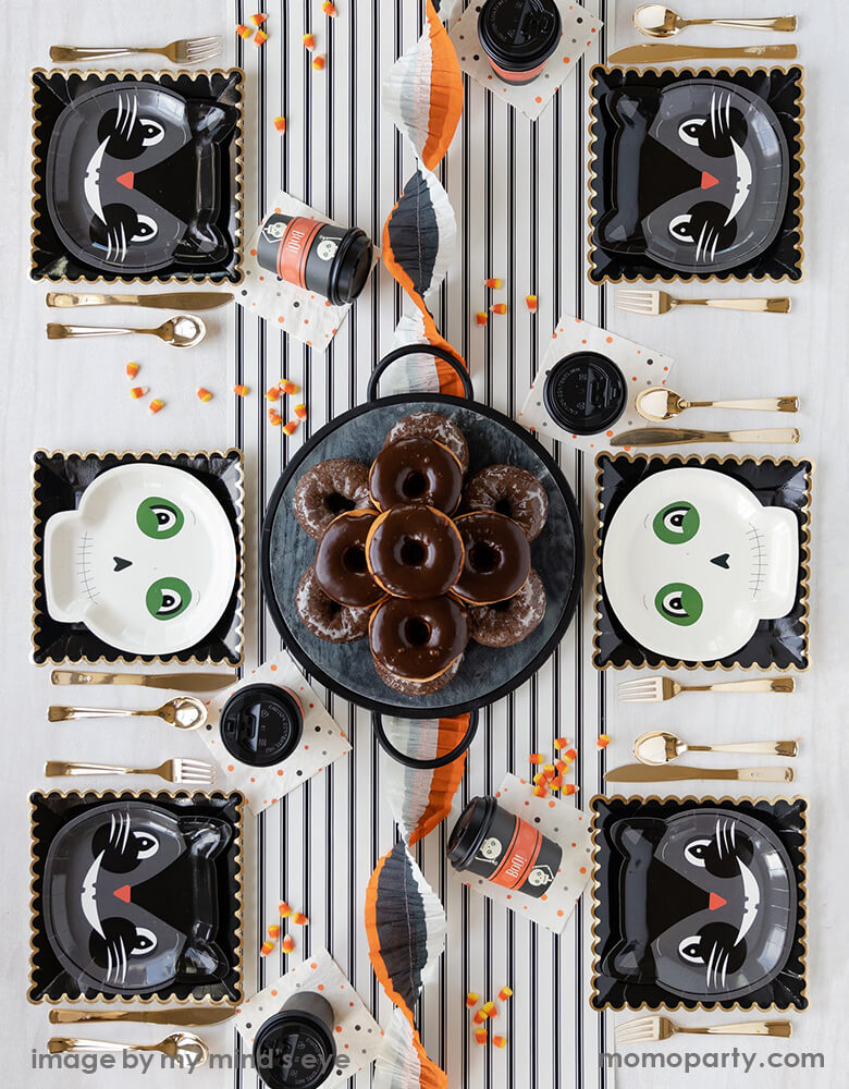 Classic vintage halloween party 6 guest table set up, with vintage halloween cat plates and SKELETON plates layered with 9 inch black scallop plates, golden untils, vintage polka dots napkins. A Cream with Black Stripe Table Runner in the middle of the table with donuts on the cake stand in the center piece. Such a vintage fun halloween party look for a kids friendly halloween party