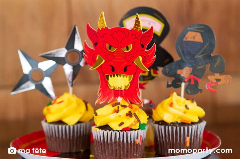 Chocolate cupcakes decorated with Momo Party's Ninja Cupcake Kit by Ma Fête.  Featuring Ninjas, Dragon head, ninja darts designs. The toppers include gold foil details to give cupcakes an eye-catching finish. They are perfect for a Ninja themed birthday party