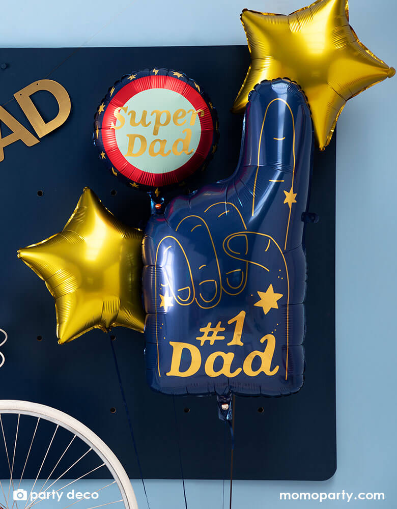 A blue wall decorated with Momo Party's #1 Dad blue finger shaped foil balloon by Party Deco and gold star shaped balloon, plus a round "Super Dad" balloon, all set a great scene for a special Father's Day celebraiton.