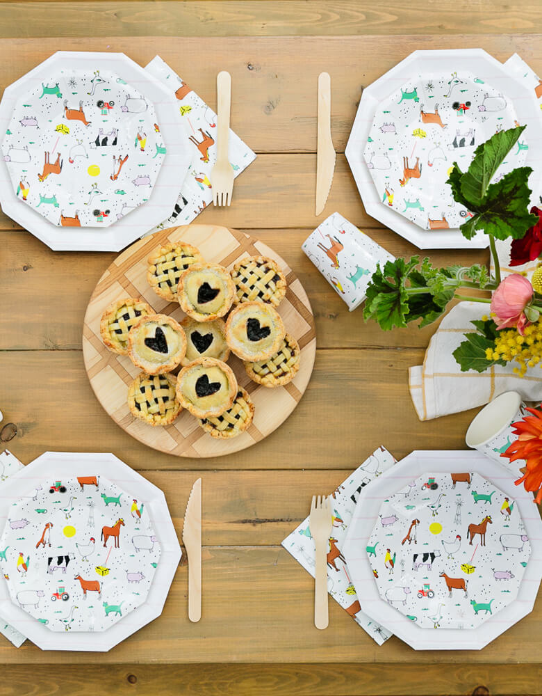 Kids Farm Barnyard Party table set up with On-The-Farm-Animals Small Plates, Napkins, wooden utensils, flowers and blueberry cookie, pies 