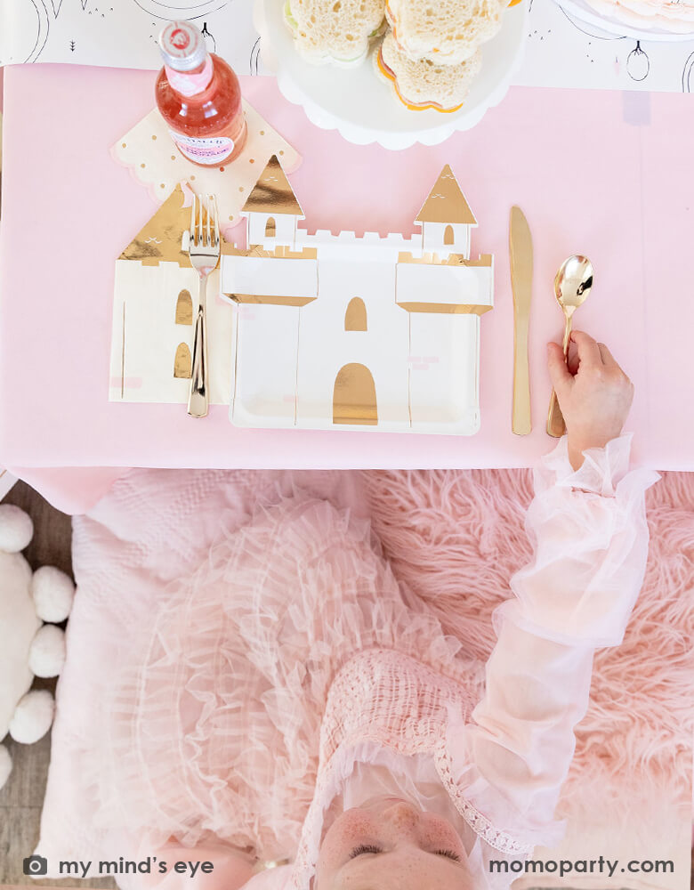 A table shot from a girl's princess themed birthday party featuring a pink party table with Momo Party's princess castle shaped plate, castle napkin and princess fairytale table runner which is a perfect party activity for a princess themed kid's party.