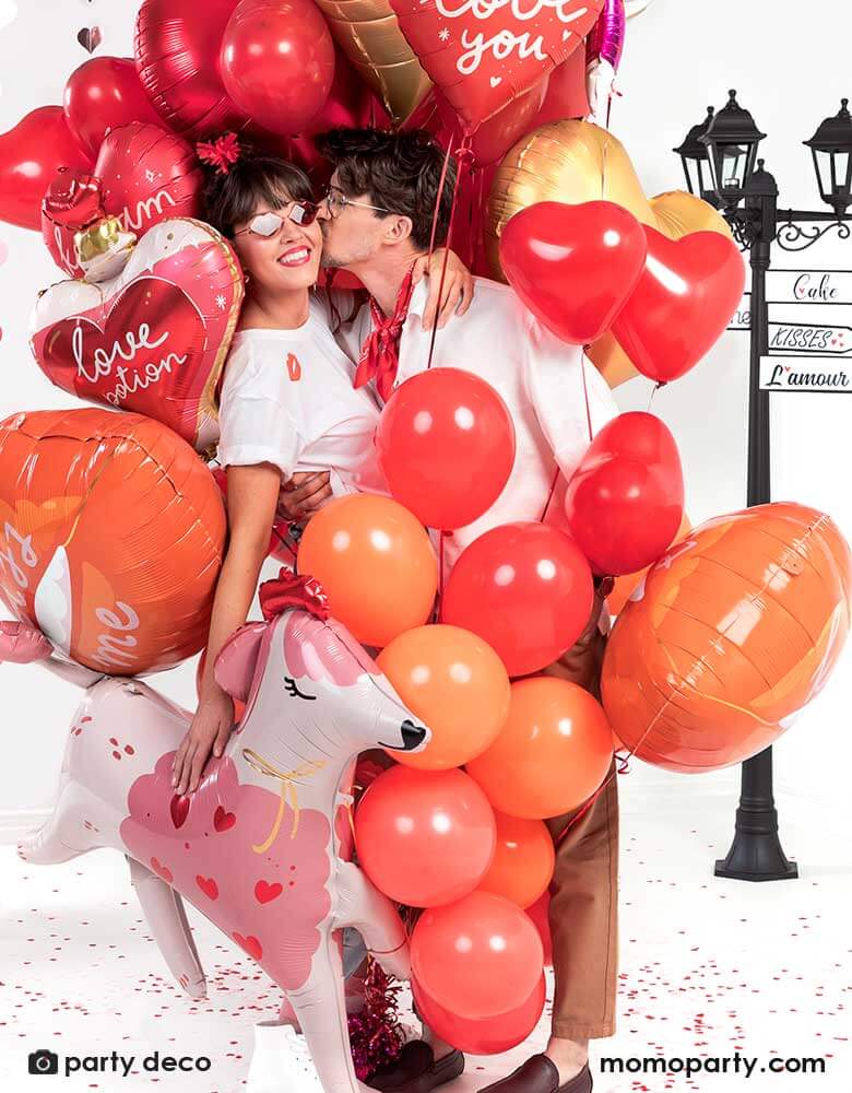 Couple kissing while holding a bouquet of Momo Party's red and pink heart-shaped balloons, celebrating Valentine's Day.