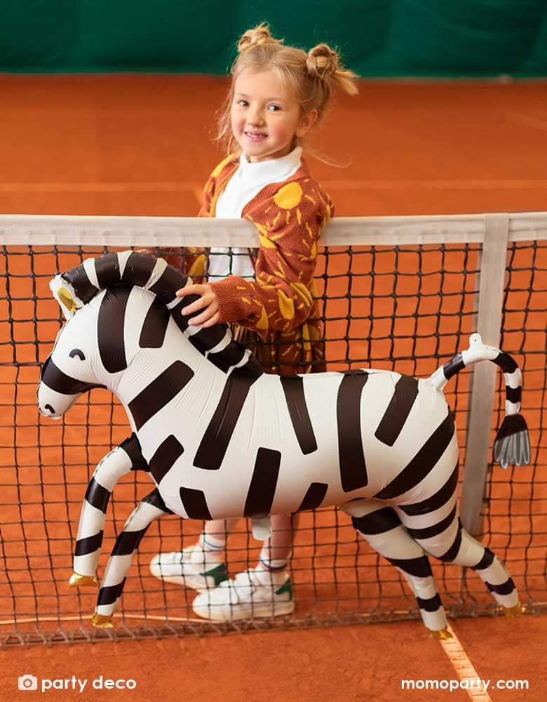 A young preschool aged girl walking along side Party Deco's 45" Zebra Foil Balloon in matte material in an outdoor tennis court
