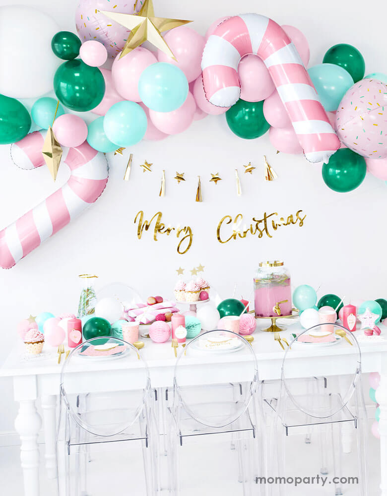Pink Christmas Party Ideas by Momo Party featuring Party Deco's Pink Candy Cane Foil Balloon on a festive balloon garland in pink, mint and green colors above a festive party table filled with Christmas themed party goods 