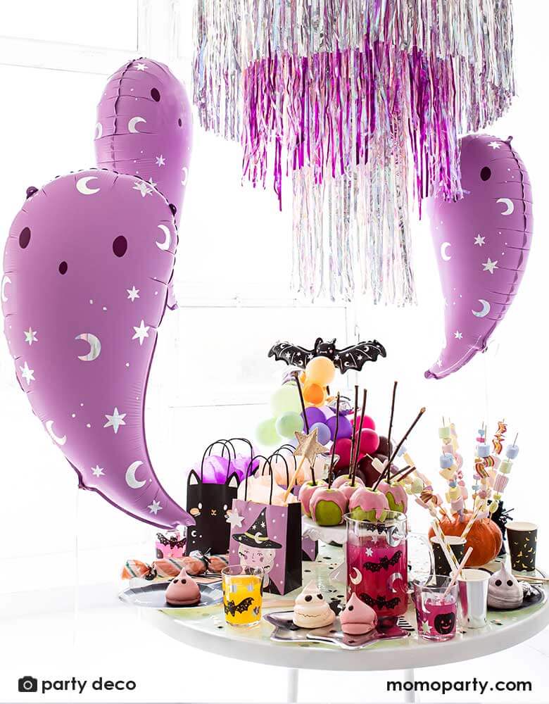 Party Deco 14 inches pink ghost foil balloons featuring iridescent moon and star icons with a party table filled with Halloween party tableware including plates, cups, napkins featuring witches, black cats. bats and ghosts  and Halloween treats and sweets, with a fringe silver and pink party garlands in the back, perfect for a not-so-scary kid-friendly pink Halloween party