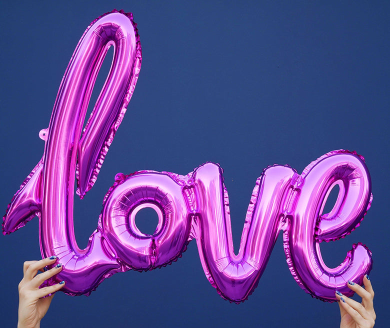Hand holding up a Pink Love Script Foil Balloon. This "love" foil balloon in script font is a perfect decoration for Valentine's Day, love themed celebrations or weddings!
