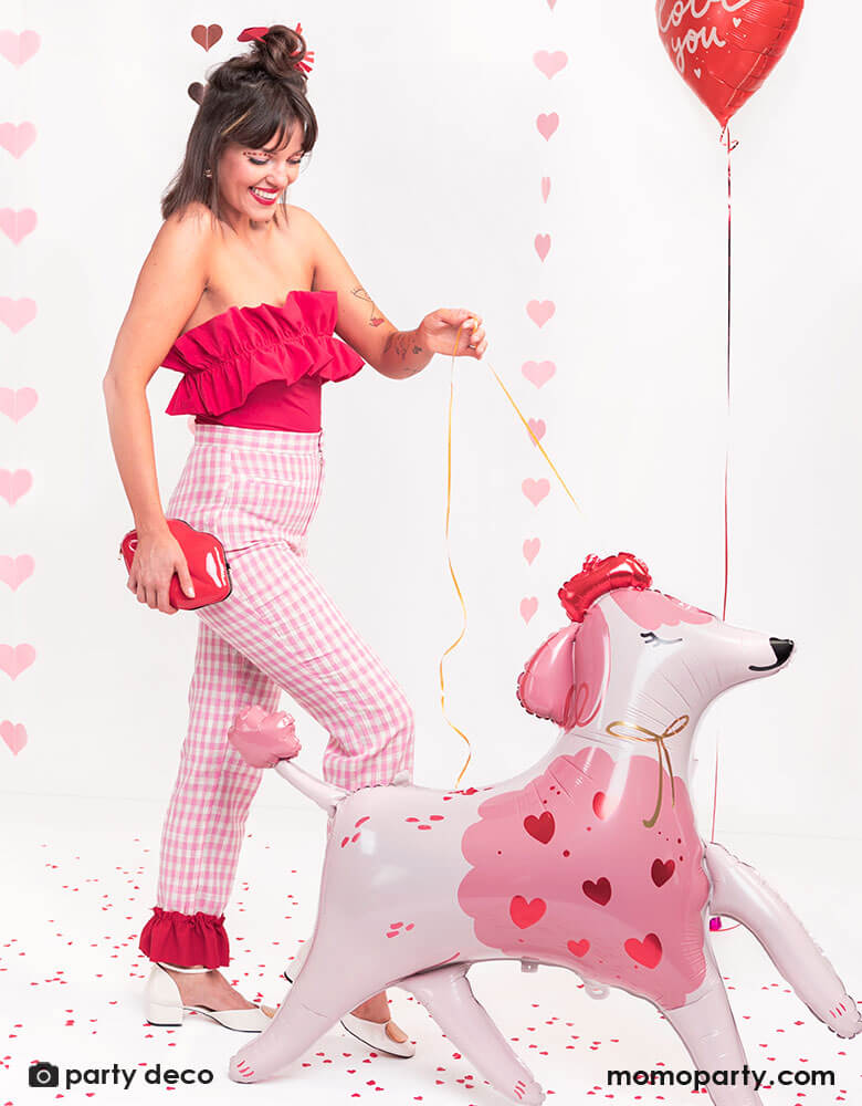 Girl in pink and red outfit happily "walking" Momo Party's 47 x 42.5 inches inches standing pink poodle shaped foil balloon by Party Deco while walking on the street, celebrating Valentine's Day