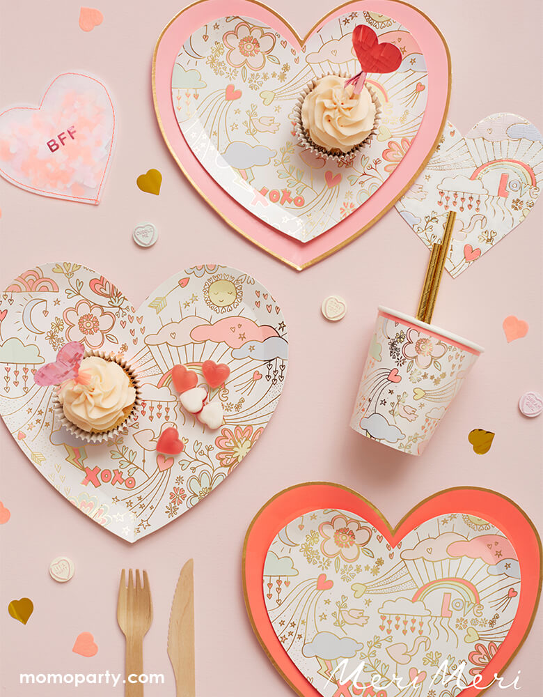 A sweet Valentine themed tablescape with Meri Meri pink tone large plates paired with Meri Meri Valentine Doodle Large Plates, cups and napkins in sweet and cute illustrations, featuring heart shaped confetti in pink and gold spread out through the table. 