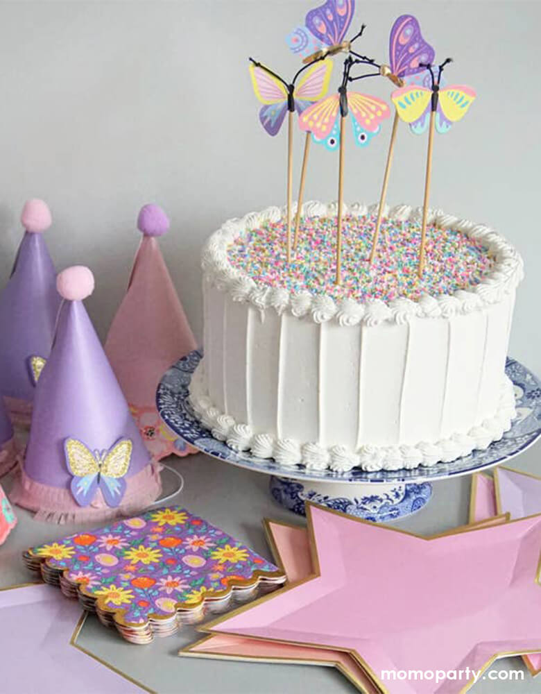 a Butterfly themed birthday party table, filled with a buttercream cake with butterfly toppers, party hats, and Pink and Peach Star Plates. These die-cut Pink and Peach Star Plates are embellished with shiny gold foil trim which adds sparkle to any stylish celebration! They're perfect for a girl power themed party or a gymnastic themed celebration!