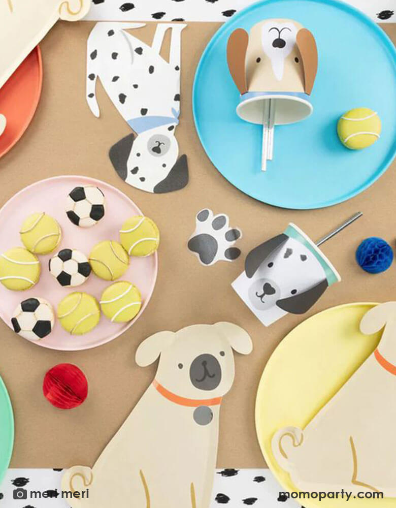 Momo Party kid's puppy dog themed birthday party table flat lay, decorated with a Pug Plate on a yellow round plate, Brown Puppy Cup with silver foil straws on sky blue colored plate, a Damatian Puppy Napkins , tennis ball macarons all on the black dots tablecloth, These modern and cute design party supplies from Meri Meri of Cat and Dog Collection,will make an Insta-perfect party table for your kid's puppy or dog themed birthday party.