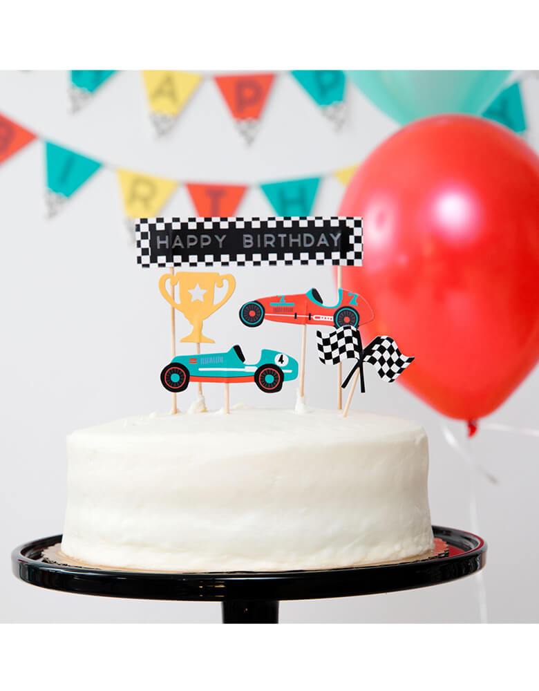 Merrilulu's Race Car Toppers on a birthday cake in a kid's race car themed party with colorful garland and balloons hung on the wall