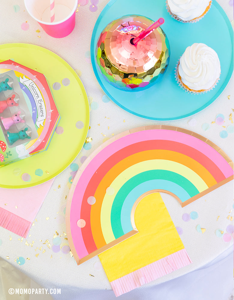 Rainbow party table view of Oh happy day rainbow plate, on top of yellow pink Hip Hip Hooray Fringe Small Napkin,  cupcakes, Rainbow Ombre Disco Ball Tumbler on top of Oh happy day Rainbow Large plates, rainbow color paper cups, confettis, Mini Unicorn Erasers as party favor for a rainbow themed birthday party