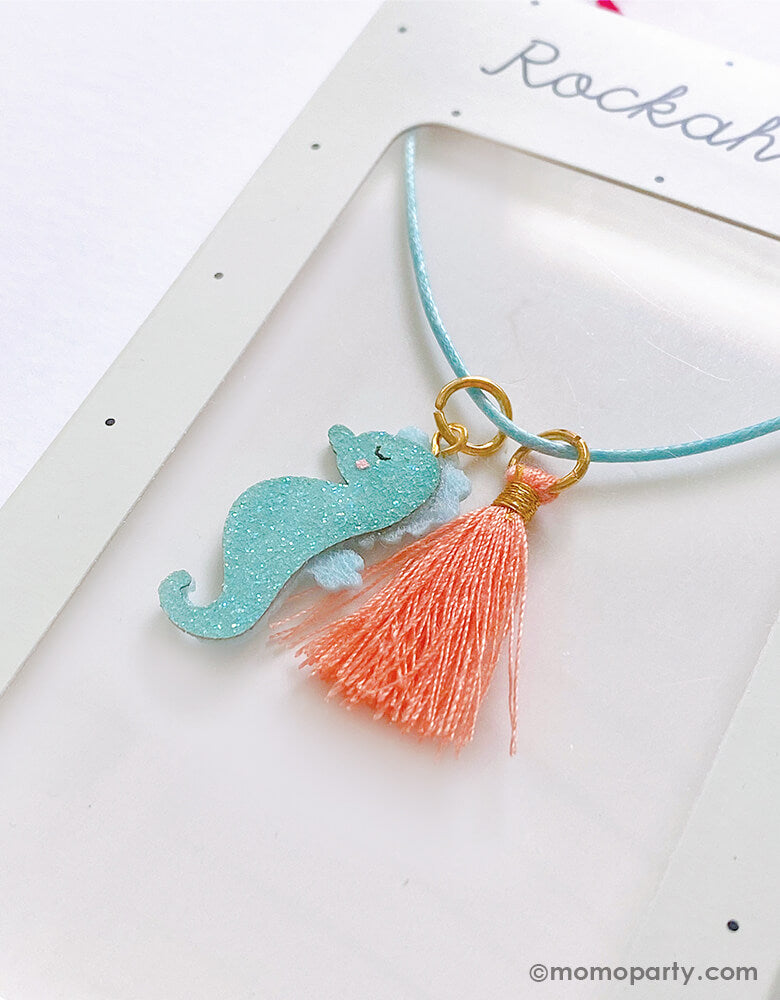 close up detail of Rockahula Kids - Sylvia Seahorse Necklace. Featuring an adorable glitter seahorse and coral tassel charm, this aqua blue satin rope cord has a lobster claw clasp on an extender chain to ensure the perfect fit for little girl