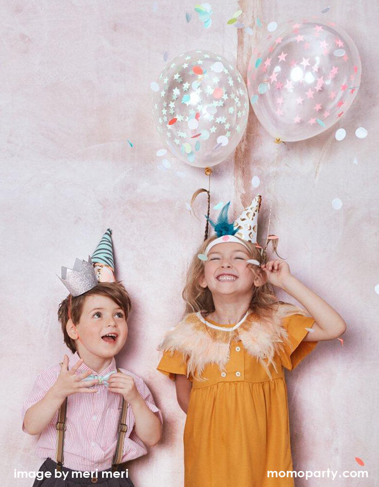 Boy and Girl having fun by dress up with feature and fun Meri Meri Party Hats with confetti balloons