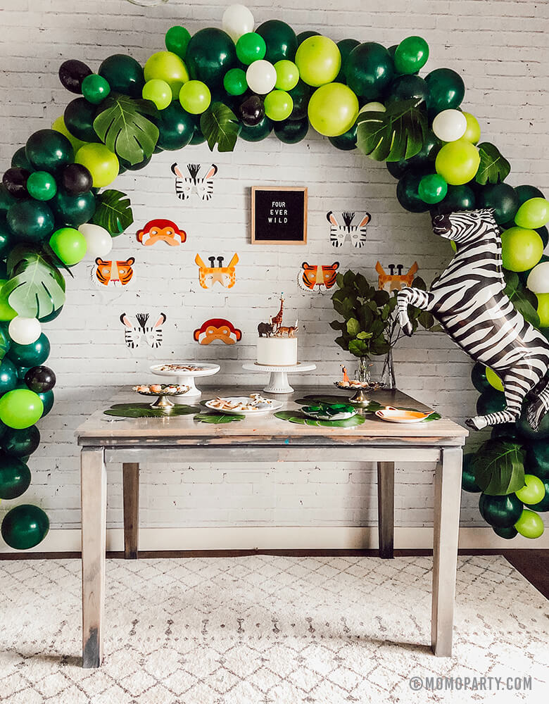 Safari Jungle Birthday Party desert table with safari themed balloon garland and Talking Tables, Party Animals Paper Masks of Zebra, Giraffe, Tiger and Monkey and letter board of "Four ever wild" sign, Zebra foil balloon on the side as backdrop wall decoration.