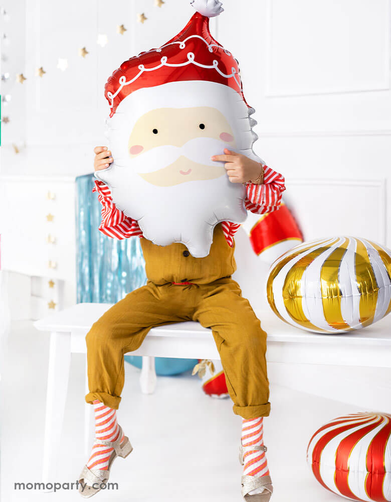 Kids Christmas Party Ideas by Momo Party featuring Party deco's 24" Santa head foil balloon held by a little girl sitting on a festive table with Christmas decorations around her