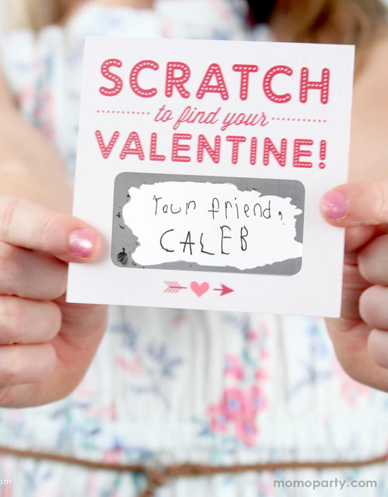 A girl holding a inklings Paperie Scratch-off-Valentines-Card, with scratched off from the her valentine gift from her friend, with a handwritten note of "your friend, Caleb" message in the blank area, Super cute card for Valentine's card exchange for the little ones, school Valentine's card exchange, Valentine's day activities, galentine's day gift