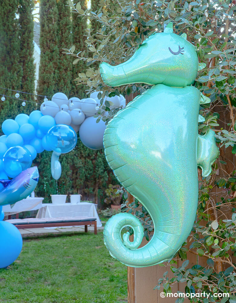 under the sea themed party at outdoor yard, a Seahorse Holographic Foil Balloon hanging in front of the entry door to welcome the guest, a blue colored balloon garland with shark foil balloon in the yard for a sea friends themed birthday party 