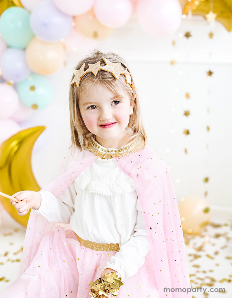 Little girl wearing a pink star sparkle cape Costume and gold Shining Star Headband, there are gold confetti in her hand just like a magical princess in a party celebration