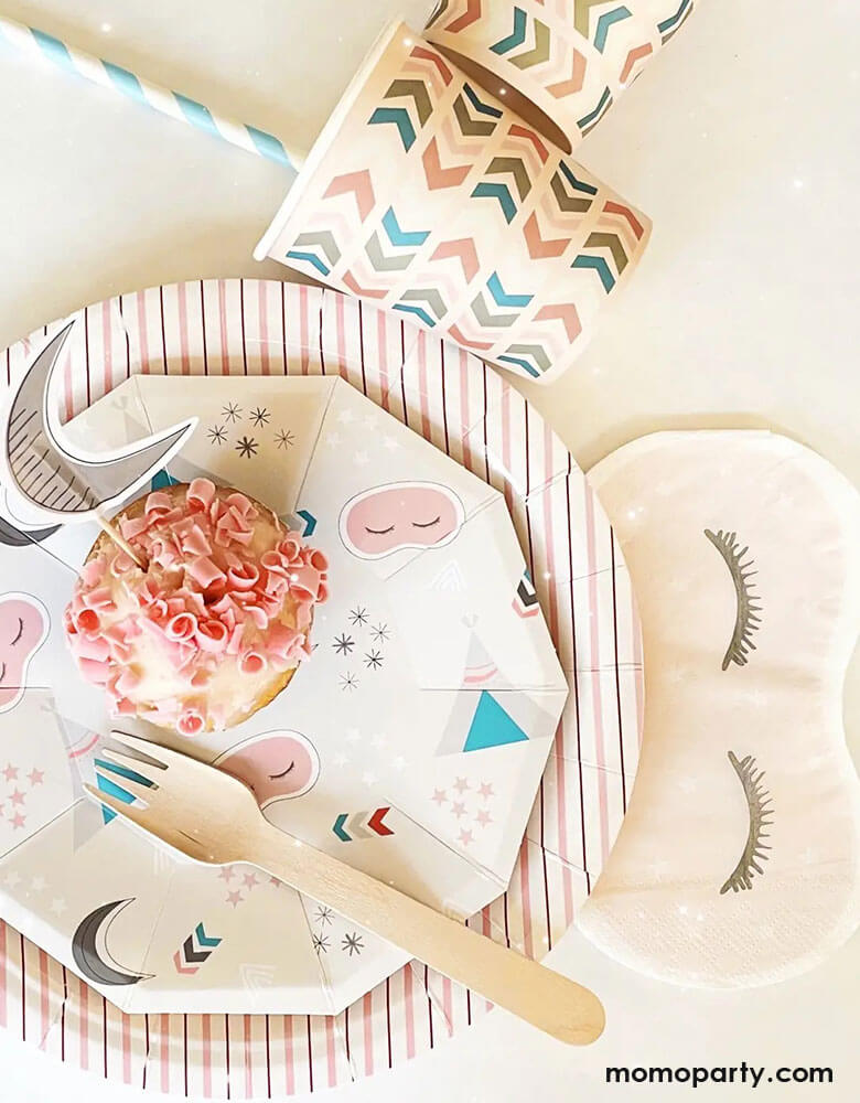 A tablescape of girls sleepover party featuring Momo Party's sleepover napkins in the shape of sleeping masks by Pooka Party, pink striped plates and light pink party cups with chevron design, perfect for girl's slumber party.