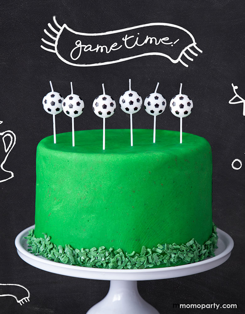 6 Party deco's soccer ball shaped birthday candles on a green cake for a soccer themed birthday party