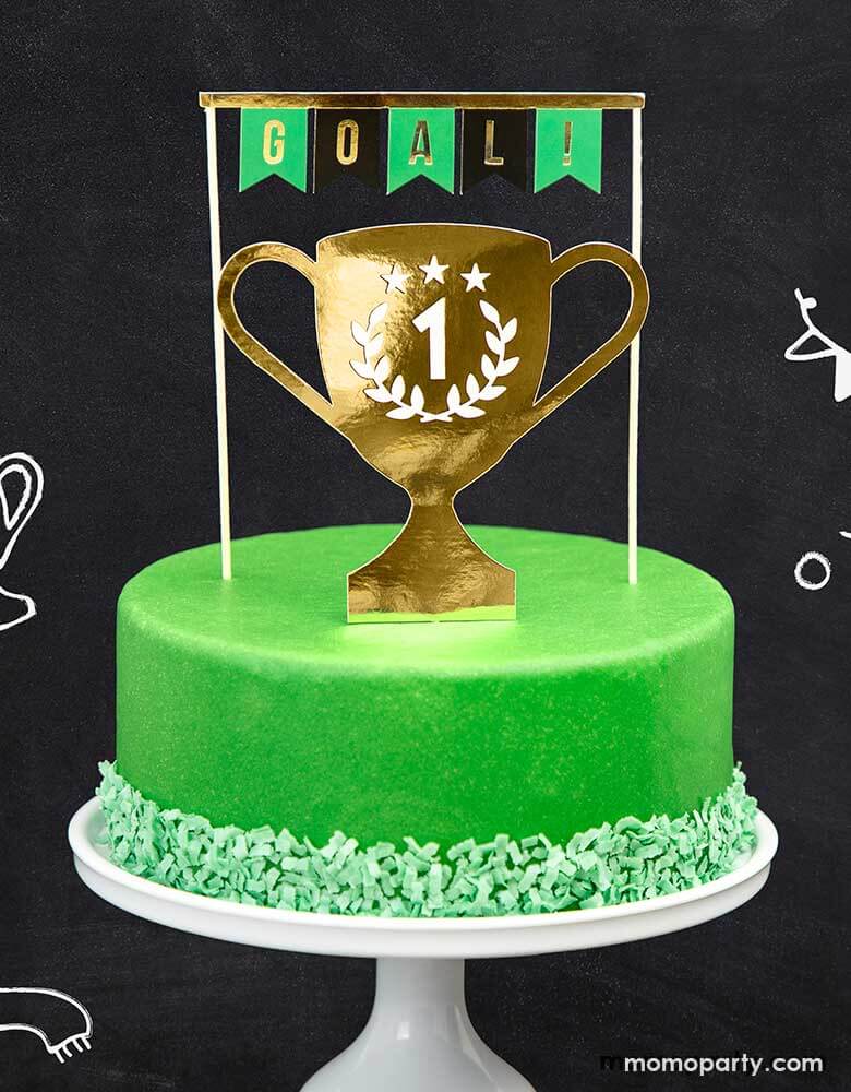 A green buttercream cake topped with Party Deco's Soccer Cake Toppers featuring a trophy cup and a bunting with "Goal!" in the classic soccer colors of black and green, perfect for a soccer themed birthday party