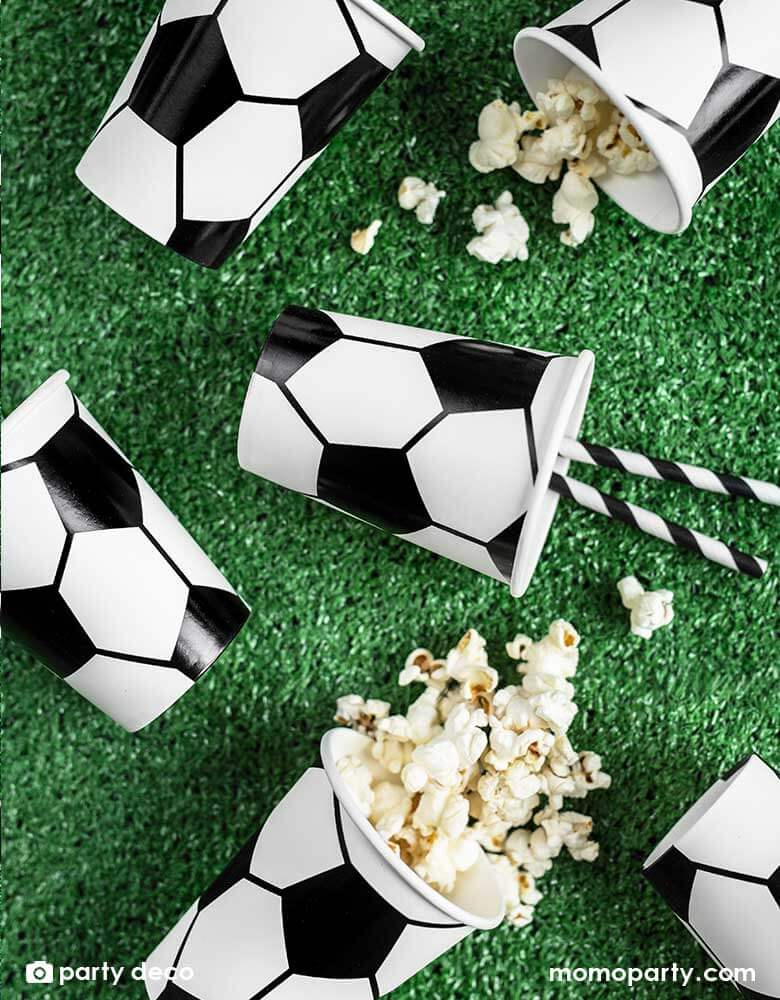 A table with Momo Party's 6.8 oz Soccer ball party cups by Party Deco in classic black and white color, perfect for a kid's soccer themed birthday party or a World Cup soccer watching party!