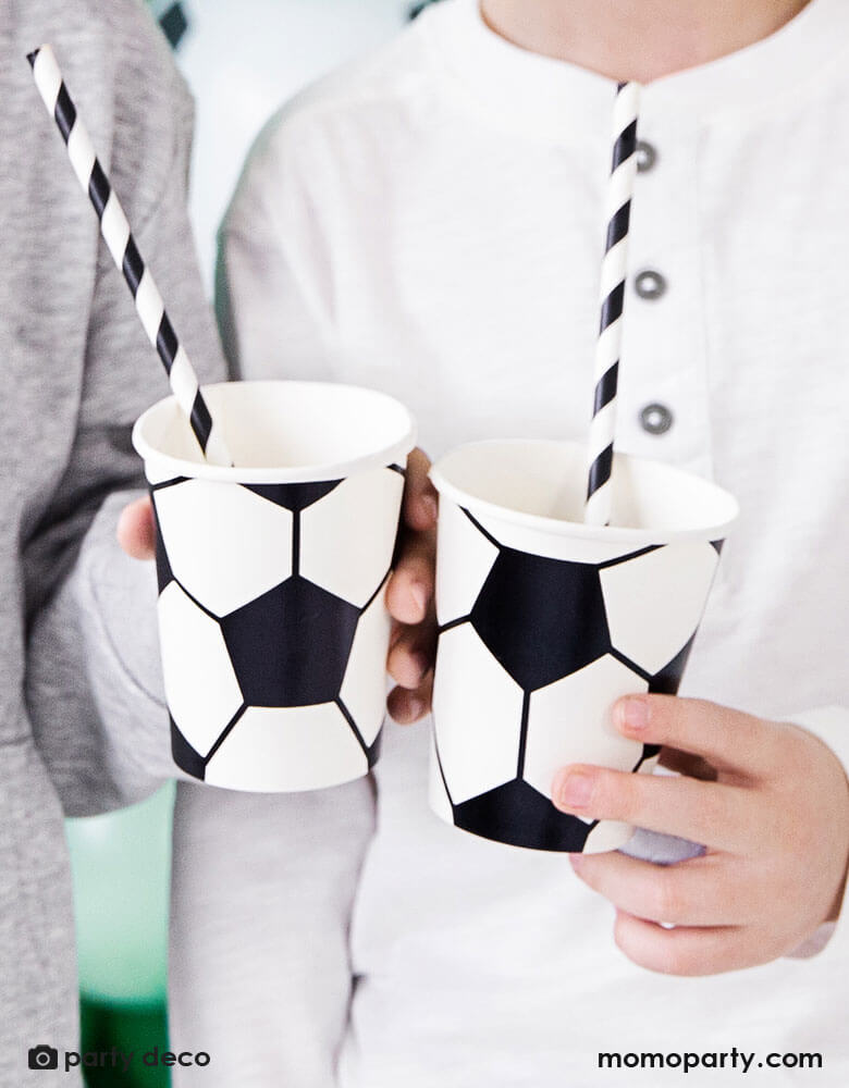 Two boys holding  Momo Party's 6.8 oz Soccer ball party cups by Party Deco in classic black and white color, perfect for a kid's soccer themed birthday party or a World Cup soccer watching party!