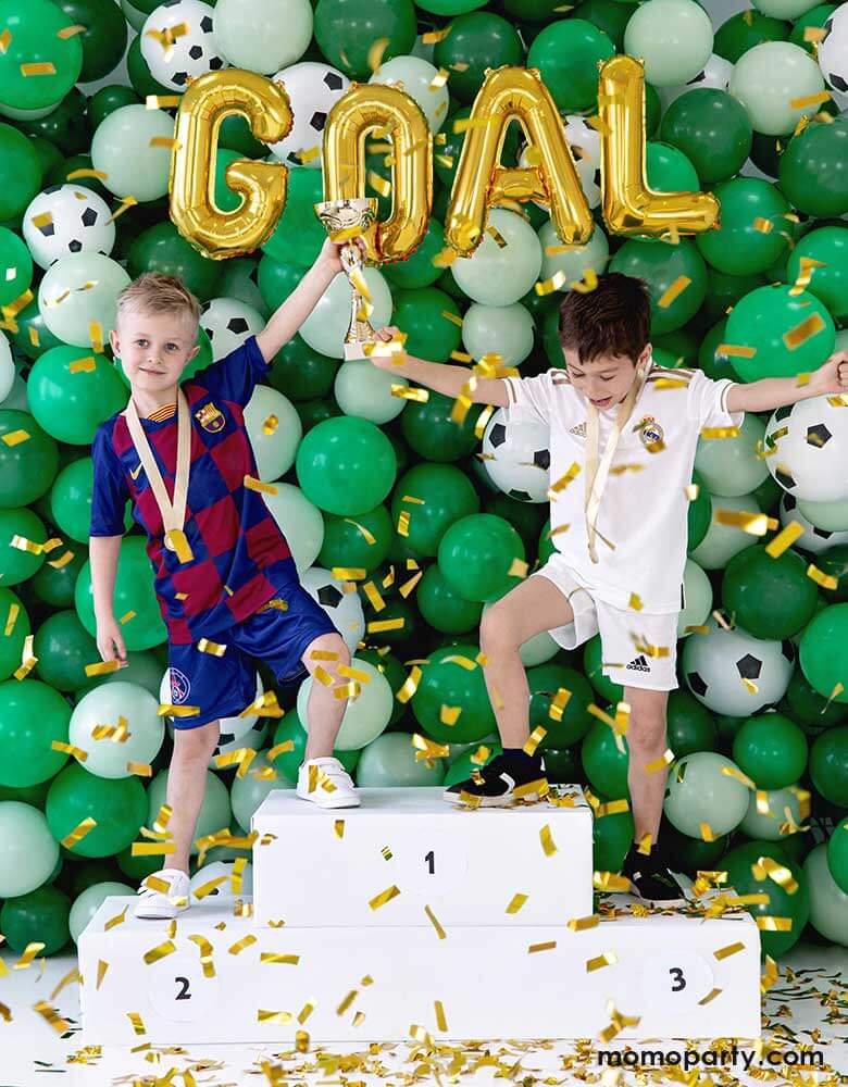 Two boys standing in front of an awesome balloon wall featuring green and mix and soccer ball latex balloons, with letter foil balloons that spell out "GOAL" perfect inspirations for soccer themed birthday party