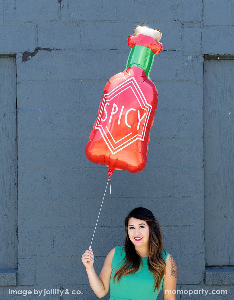 Lady wearing green dress holding a Jollity & co. 36 inches Spice Bottle Foil Mylar Balloon. is the perfect thing to add a little spice to your next fiesta!