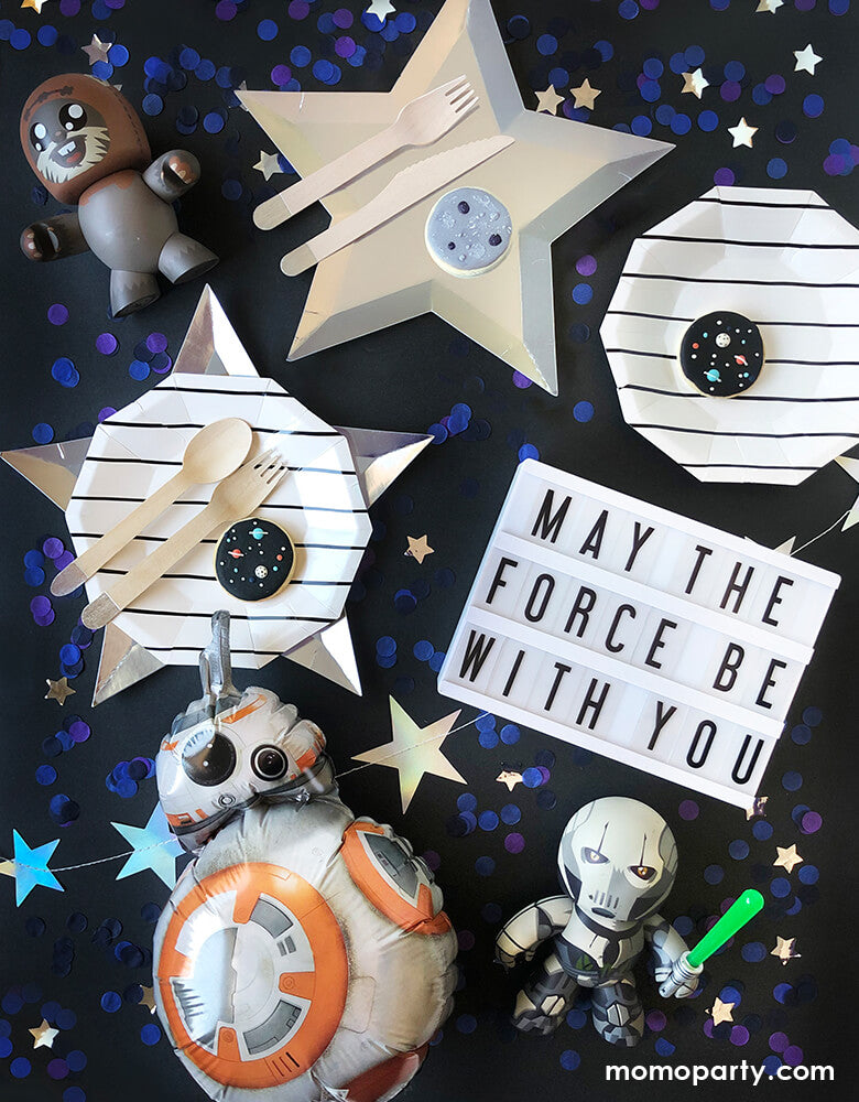 "May the force be with you" Star Wars themed party table filled with Meri Meri Star Silver Foil Plates, Day Dream Society Black Striped Small Plates, Star Wars BB8 Mini Foil Balloon, Rocket Stars Banner, star war toy figures, and blue purple starts confetti for a modern star war birthday party
