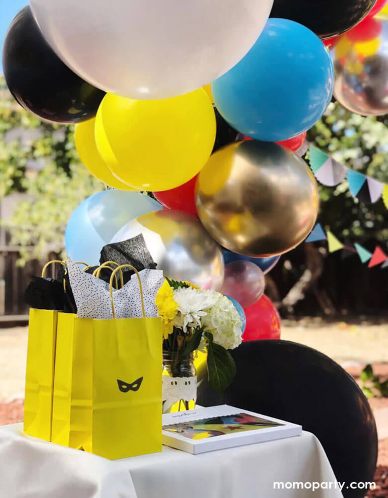 A kid's superhero party set up by Momo Party with a colorful balloon cloud in bright vibrant colors and superhero themed birthday banner, in the front of the table was a few goodie bags with a superhero mask stamp on it, a great way to great a superhero themed goodie bag in a modern way! 